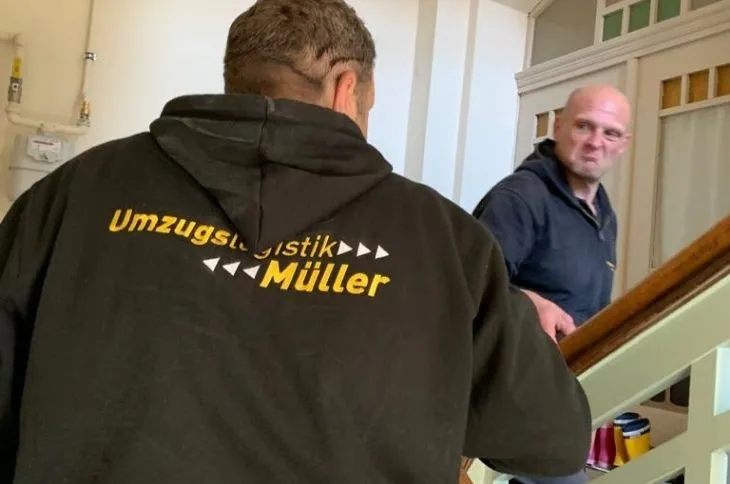 zwei umzugshelfer tragen moebel durch treppenhaus